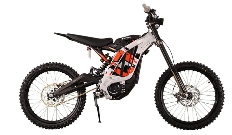 Side view of an electric dirt bike with a white and black frame, off-road tires, and orange graphics. The bike is equipped with front and rear suspension.