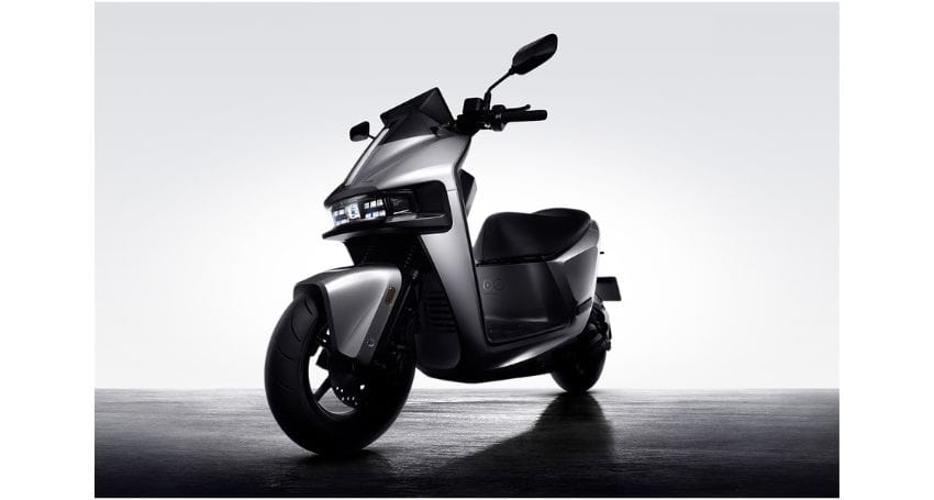 A silver electric scooter is parked on a concrete surface against a plain white background.