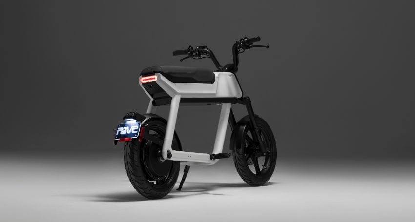 A modern, sleek electric bike with a minimalist design is shown with a black and white color scheme on a gray background. The rear light is visible, and the bike has thick tires and handlebars.