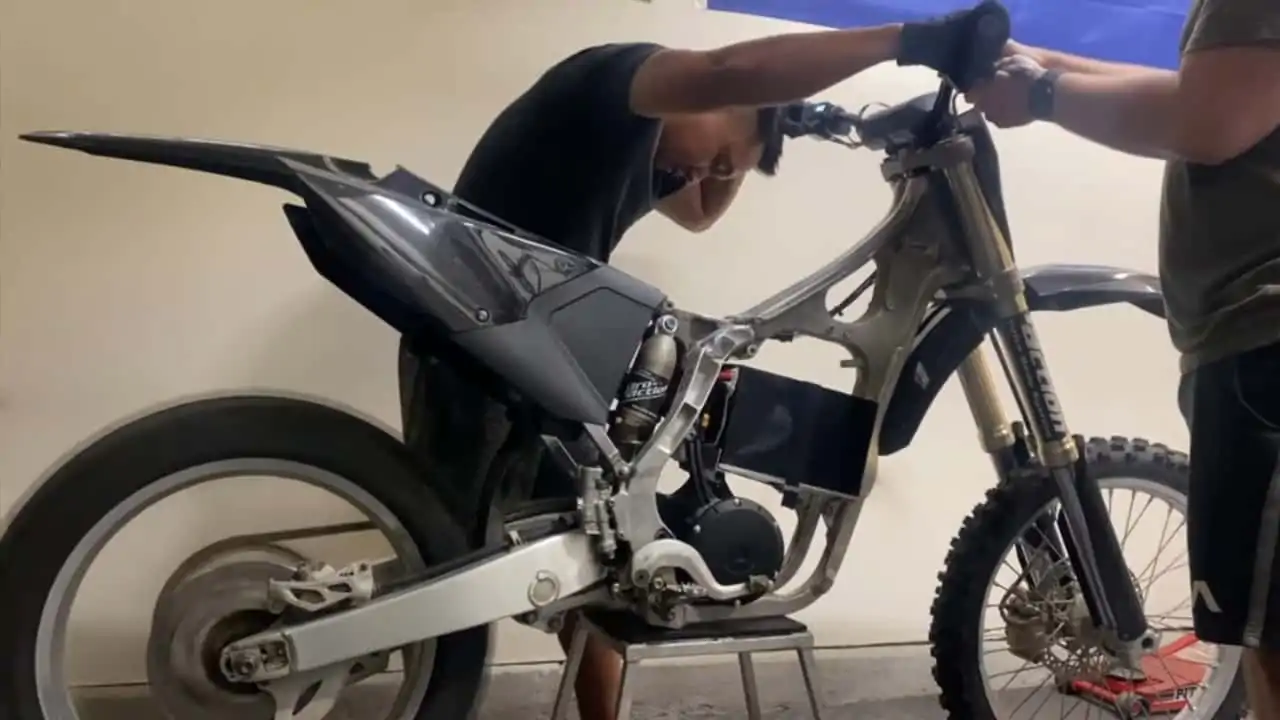 A person working on a partially assembled motorcycle, focused on the handlebars and front section, indoors.