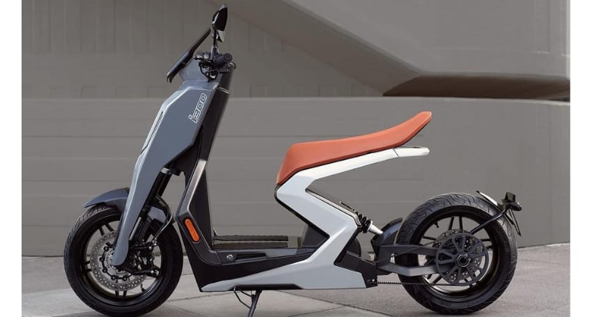 Side view of a modern electric scooter with a sleek gray and white body and an orange seat, parked against a neutral background.