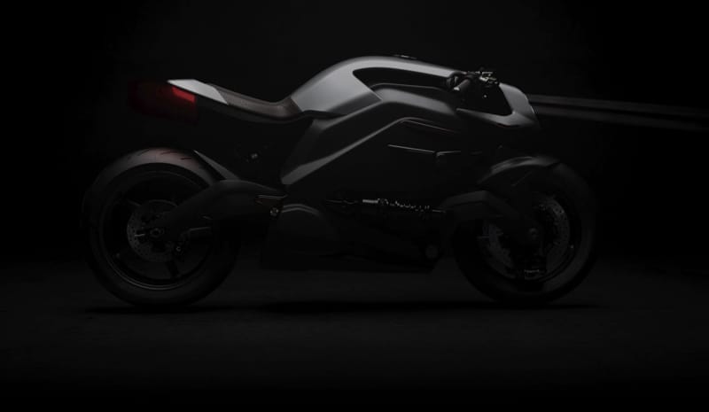 A black motorcycle with a sleek, futuristic design is shown in a dark setting, highlighting its contours and details.