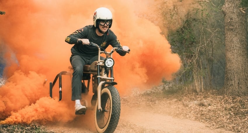 Person riding a Limited Edition EV tricycle with a trail of orange smoke behind them.