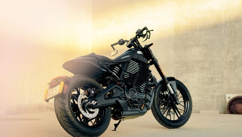 Black motorcycle parked against a textured wall with warm lighting.