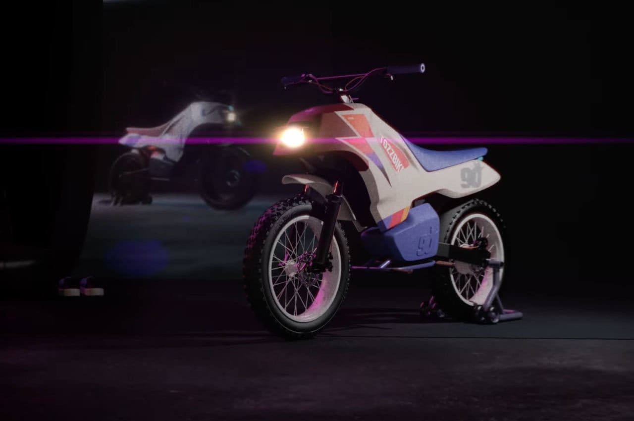 A dirt bike with a digital display on a dark stage is illuminated by a spotlight, with a reflection of the bike seen in the background.