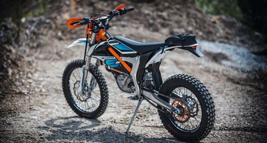 A blue and orange dirt bike parked on a dirt road.