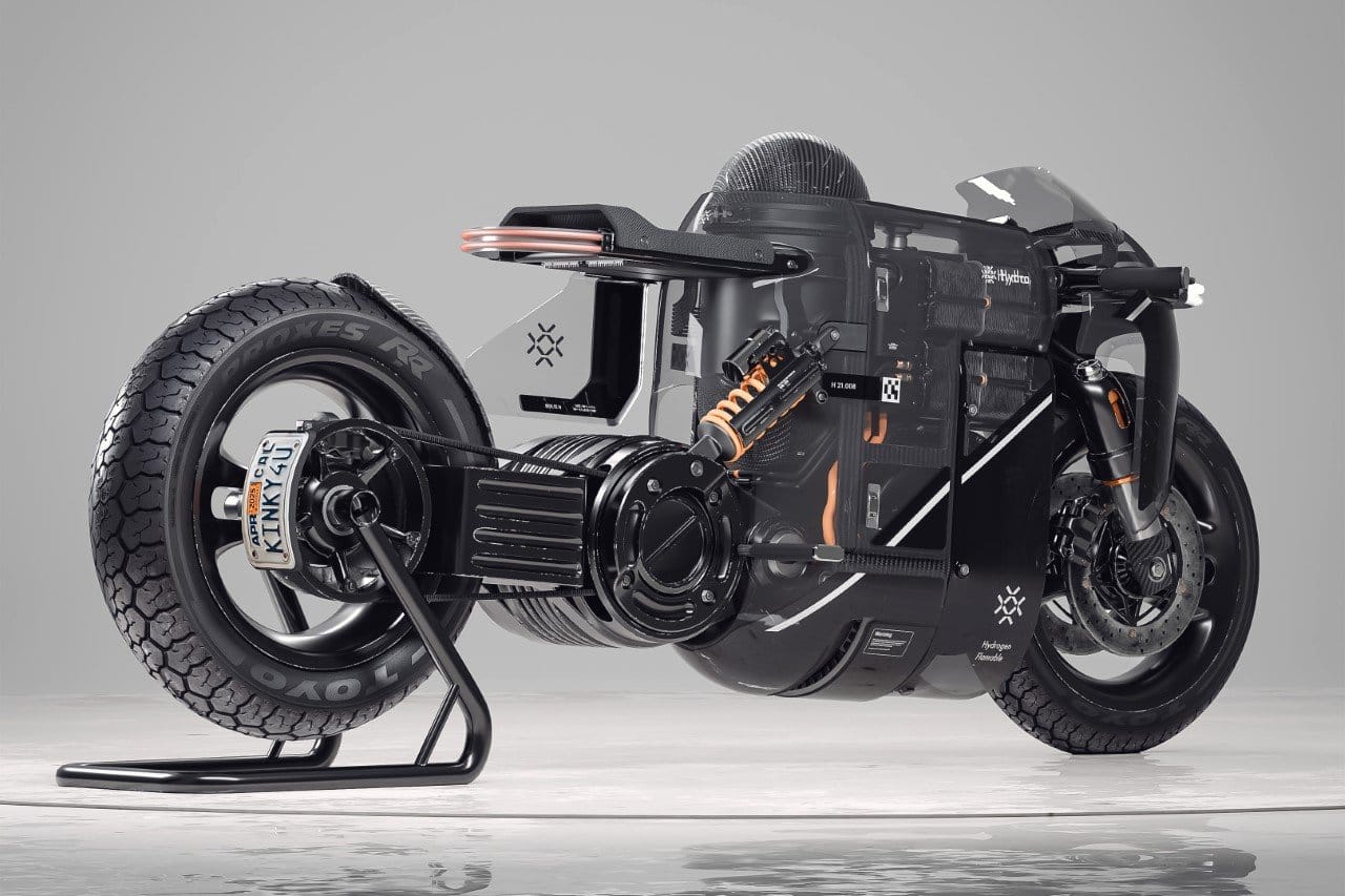 Futuristic motorcycle with exposed mechanical components and a sleek, minimalist frame on display, featuring large off-road tires and an upright stand.