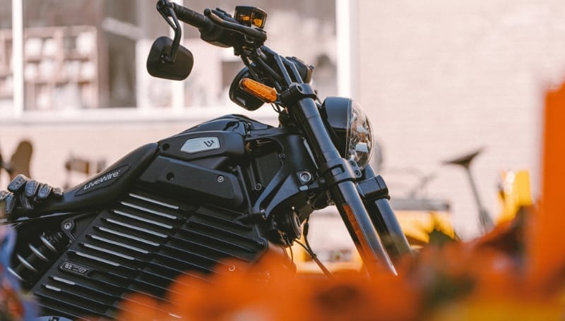 A close-up of a modern motorcycle with a distinctive black engine and handlebars, framed by orange flowers in the foreground.