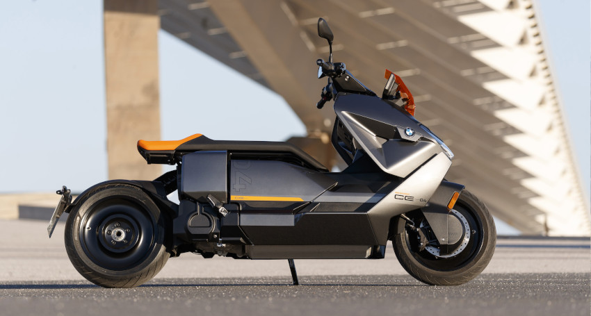 Side view of a sleek, modern, grey BMW electric scooter parked on a concrete surface, with an architectural structure in the background.