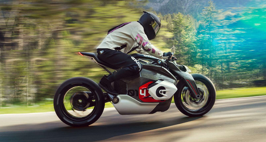 A person wearing riding gear and a helmet rides a sleek Vision DC Roadster on a road, surrounded by blurred greenery, indicating motion.