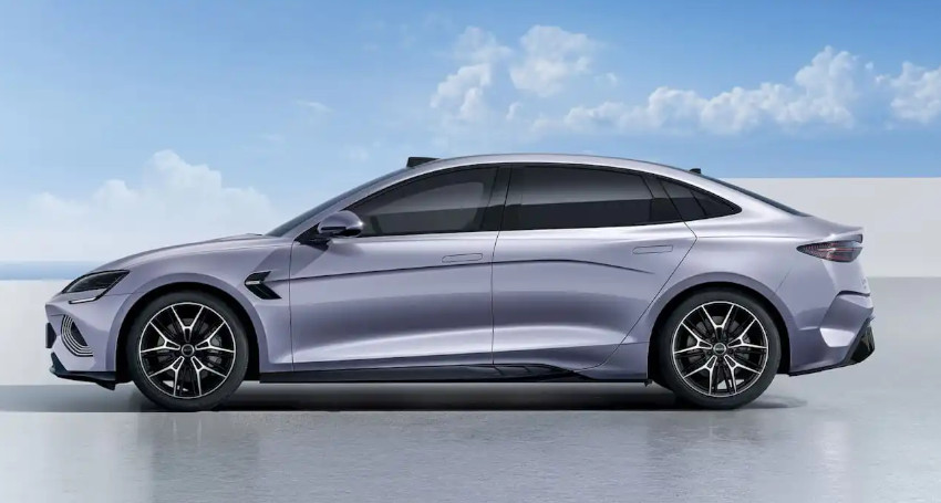 A sleek, silver sedan with black-tinted windows is parked on a reflective surface under a blue sky with scattered clouds.