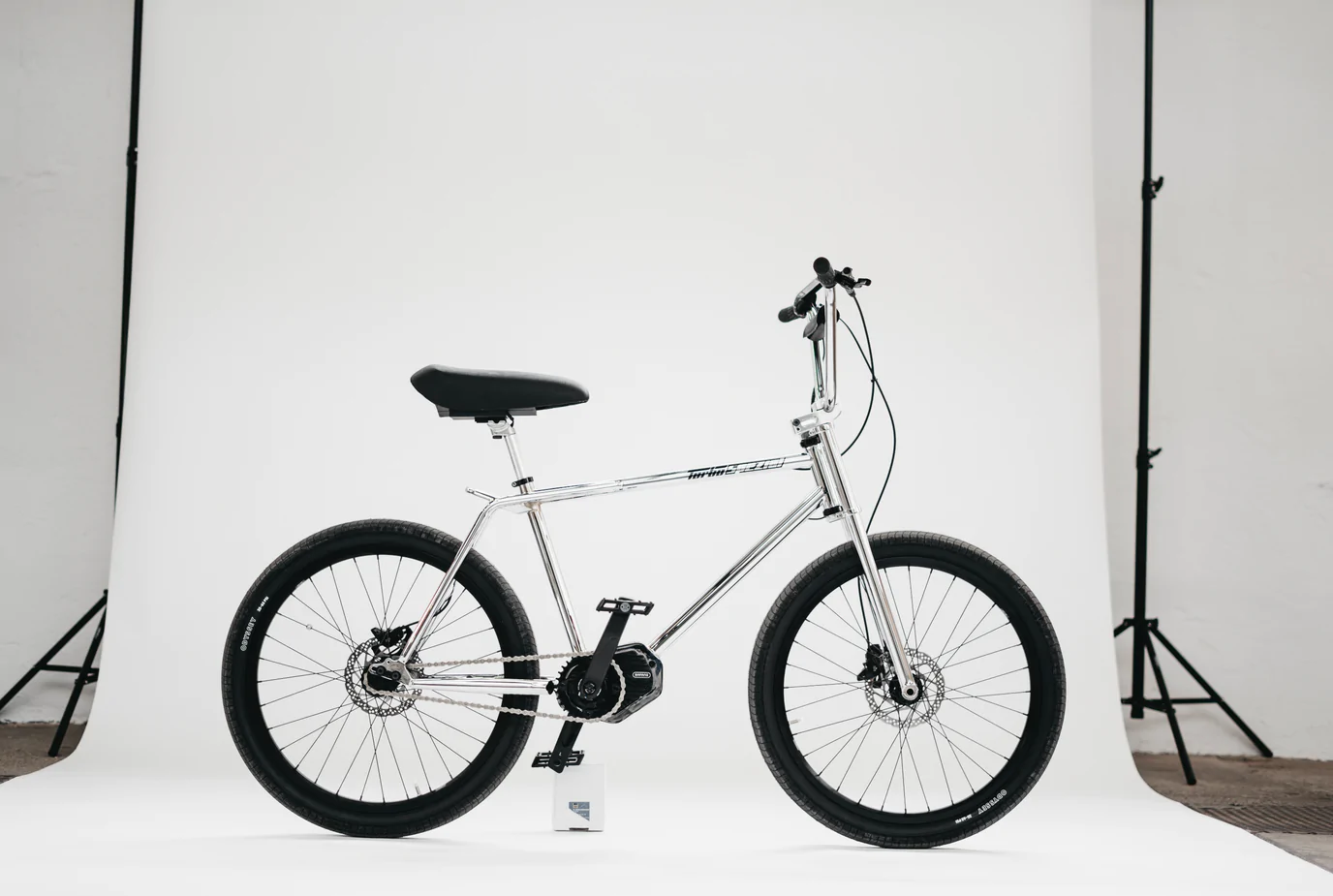 A silver BMX-style bicycle with black handlebars, seat, and wheels is positioned against a plain white background.