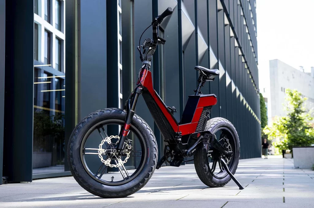 A red and black electric bike parked in front of a building.