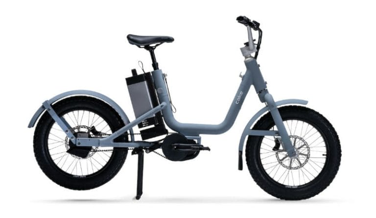 A grey electric bicycle with front and rear disc brakes, thick tires, and a visible battery pack mounted to the frame. The bike has a step-through frame for easy access.