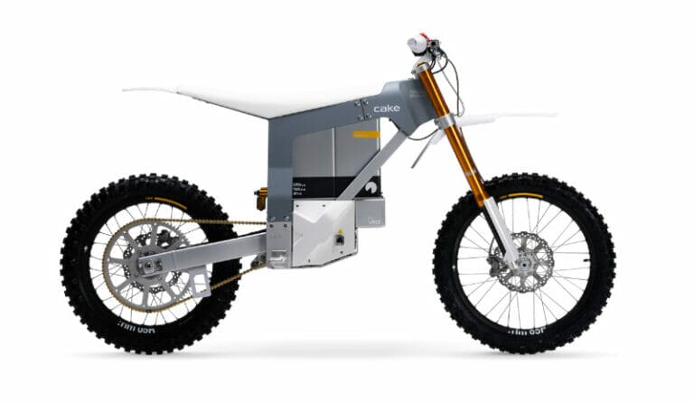 A side view of a Cake Kalk electric motorcycle with a minimalist design, featuring off-road tires and a sleek gray and white color scheme.