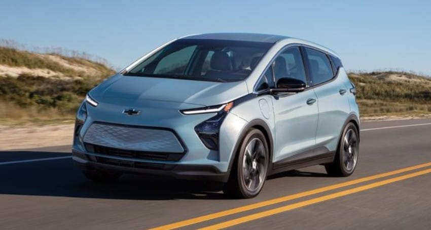 A silver chevrolet bolt ev driving on a sunny highway, showcasing its modern design and compact shape.