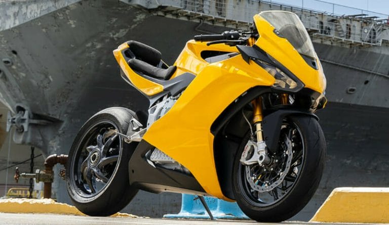 A bright yellow sport motorcycle is parked on a concrete surface in front of a large, grey, industrial structure.