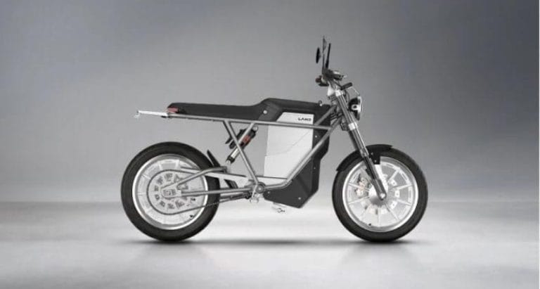 Side view of a modern electric motorcycle with a minimalist frame design, silver and black color scheme, and large wheels, displayed against a plain gradient background.