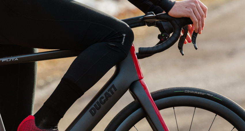 Close-up of a person gripping the handlebars of a Ducati Futa E-Bike while riding, showcasing the sleek bike's frame and front tire.