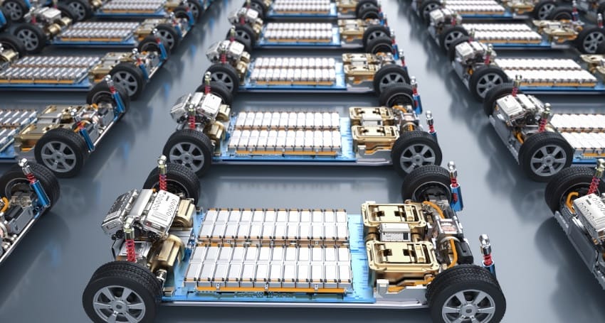 Rows of electric vehicle chassis with exposed battery packs and motors displayed in a production setting.