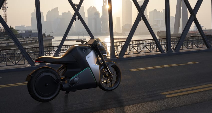 A sleek, futuristic motorcycle parked on a bridge with a city skyline in the background during sunset.