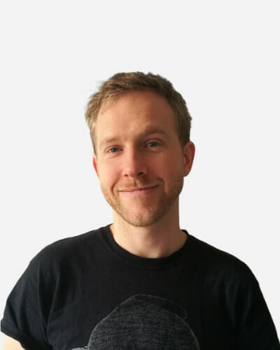 Man with short hair and a beard, wearing a black T-shirt, standing against a plain white background.