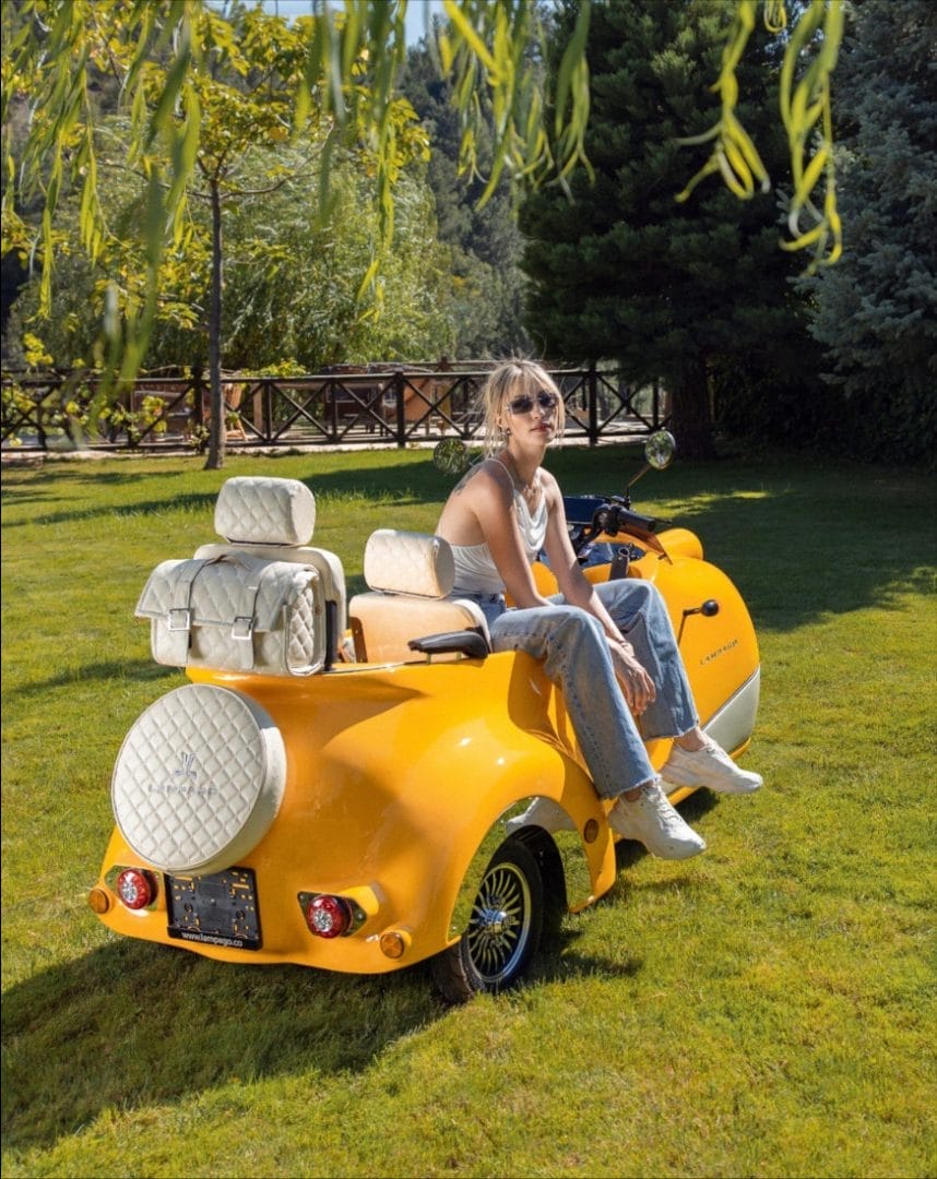 A woman is sitting on a yellow scooter in a grassy area.