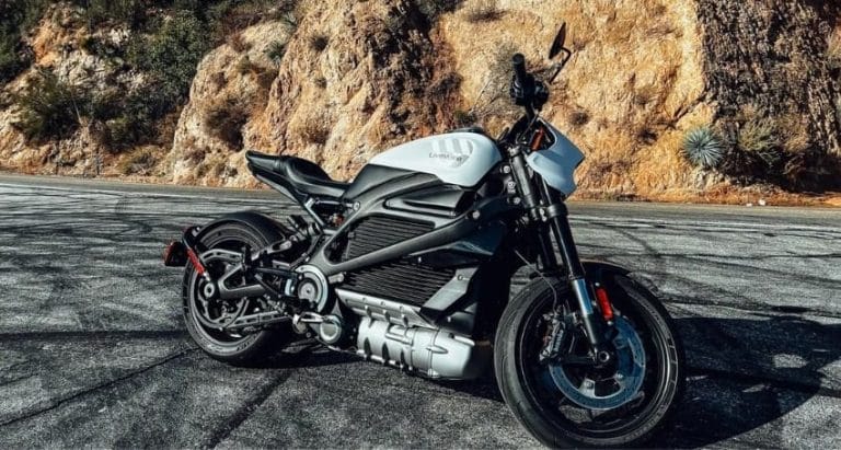 A black and white electric motorcycle parked on a paved road with rocky hills in the background.