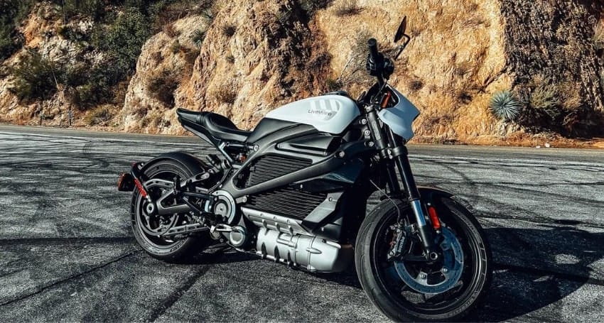 A black and white electric motorcycle parked on a paved road with rocky hills in the background.