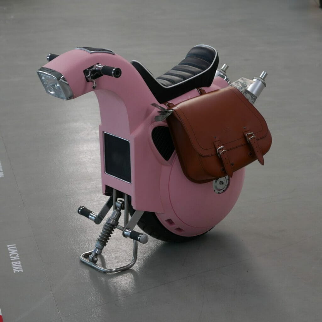 A pink motorcycle with a brown bag on it.