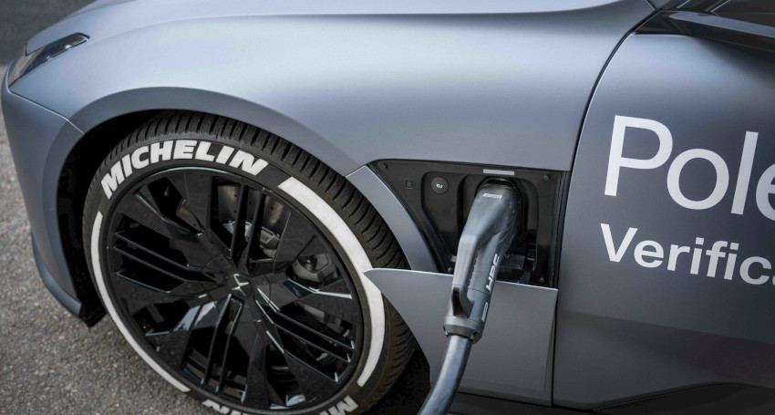 An electric car, featuring a Michelin tire, is benefiting from a charging breakthrough as it powers up at a station. The charging port is conveniently located on the front fender.