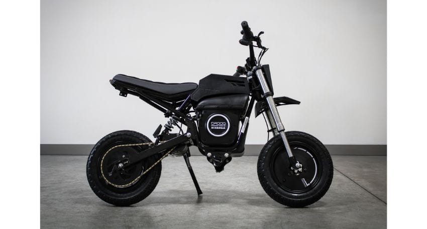 A black electric minibike with a kickstand, displayed on a concrete floor against a plain white wall.