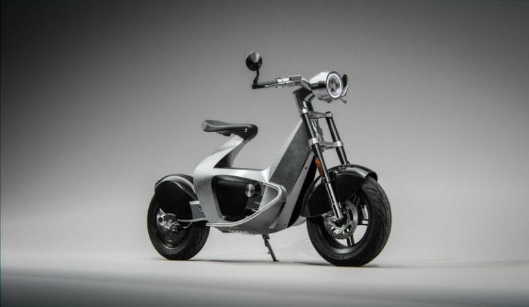 A modern, silver electric scooter with a minimalist design, featuring a round headlight, black seat, and two wheels, displayed on a plain gray background.