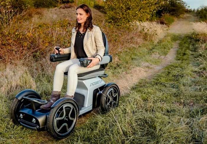 A woman rides a mobility scooter in a field.