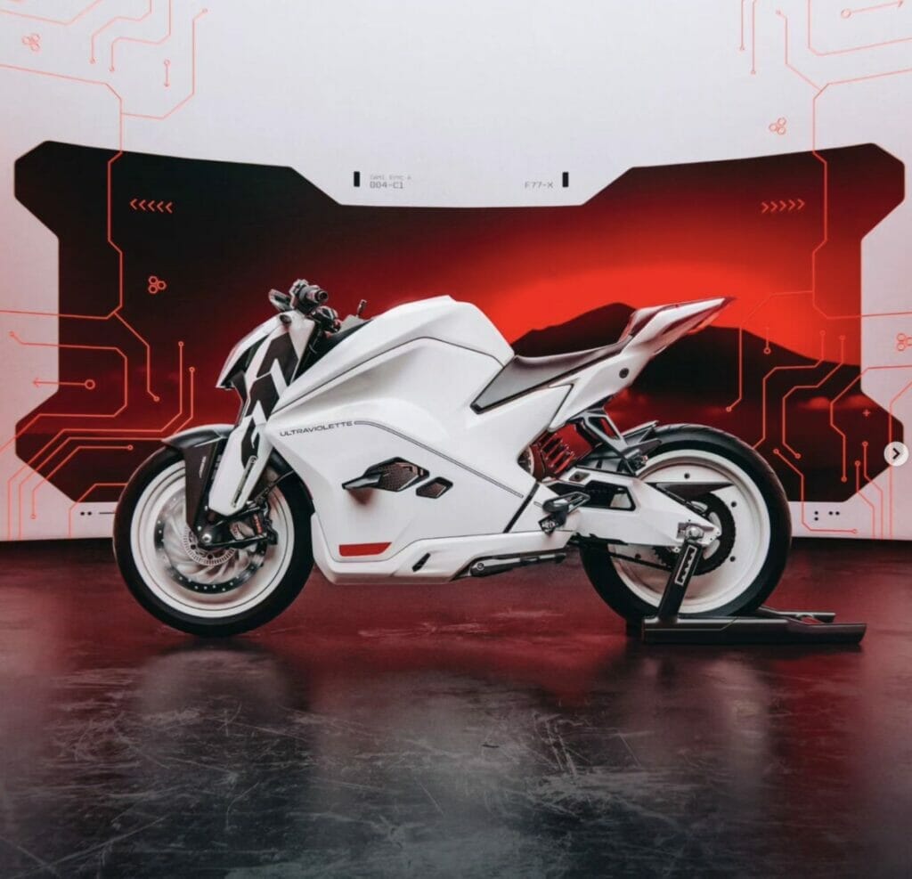 The Ultraviolette F77, a white motorcycle, is parked in front of a red background, holding the Long-Distance Electric Motorcycle Record.