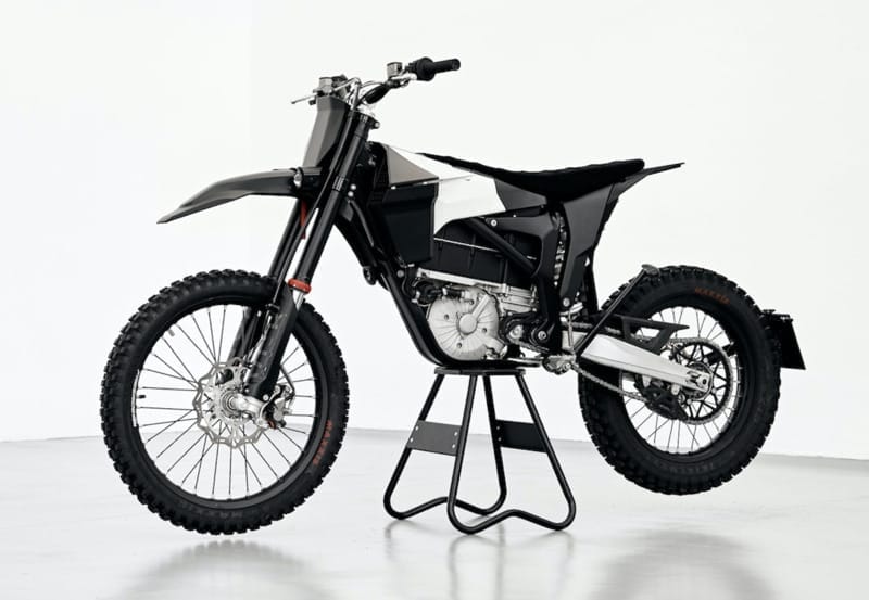 A black and white off-road motorcycle is displayed on a stand in a bright, white room.