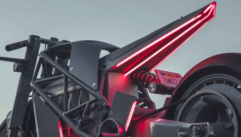 A close-up view of the rear section of a futuristic motorcycle, featuring angular design elements, exposed mechanical parts, and red accent lights.