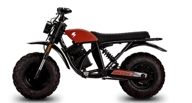 A side view of a black and orange electric off-road motorcycle with large knobby tires and a minimalistic frame.