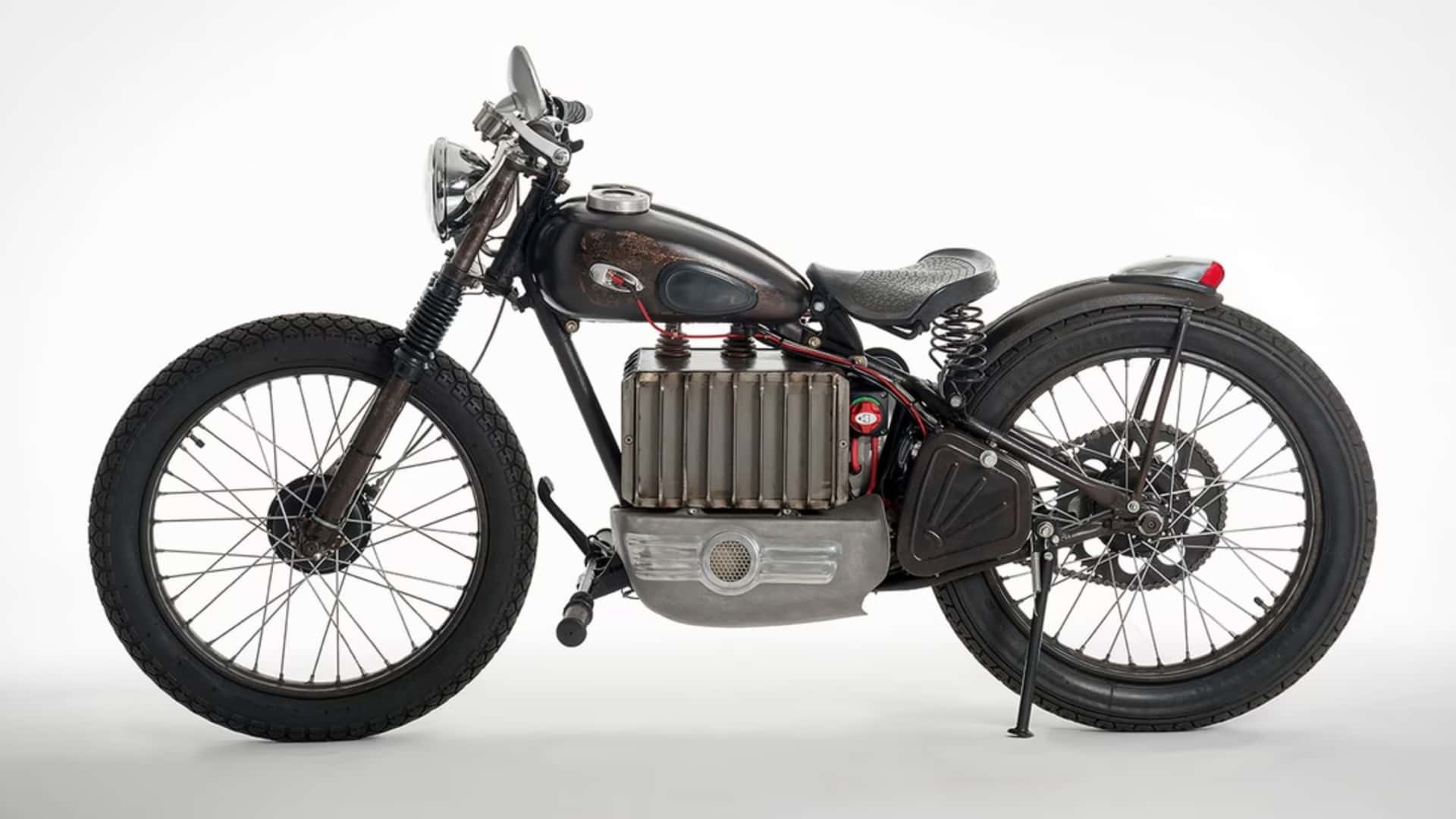 A vintage-style motorcycle with a dark, sleek body, large cylindrical engine, and thin seat, displayed on a white background.