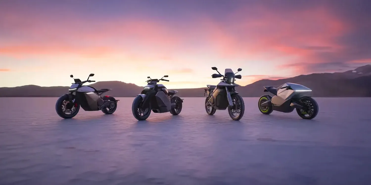 Four futuristic motorcycles parked on a flat, open area at sunrise or sunset, with mountains in the background.