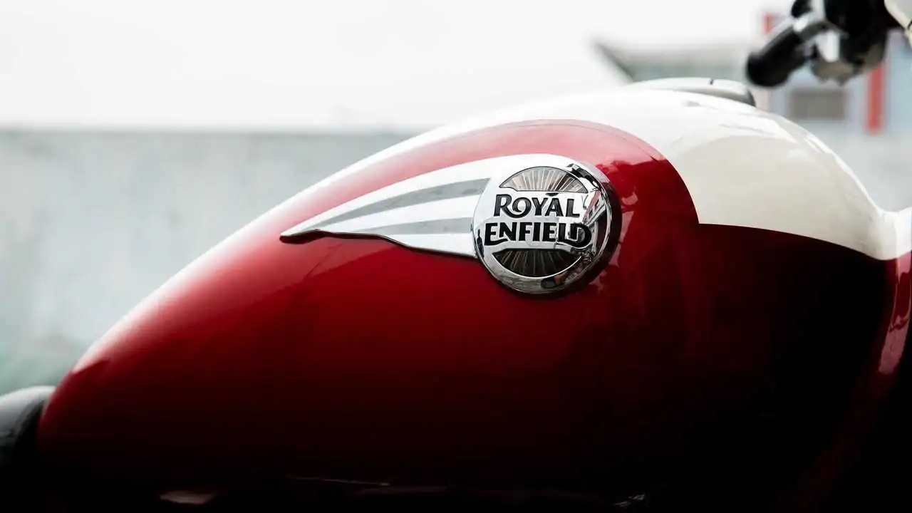 Close-up of a Royal Enfield motorcycle's red and white fuel tank with the brand's logo prominently displayed.