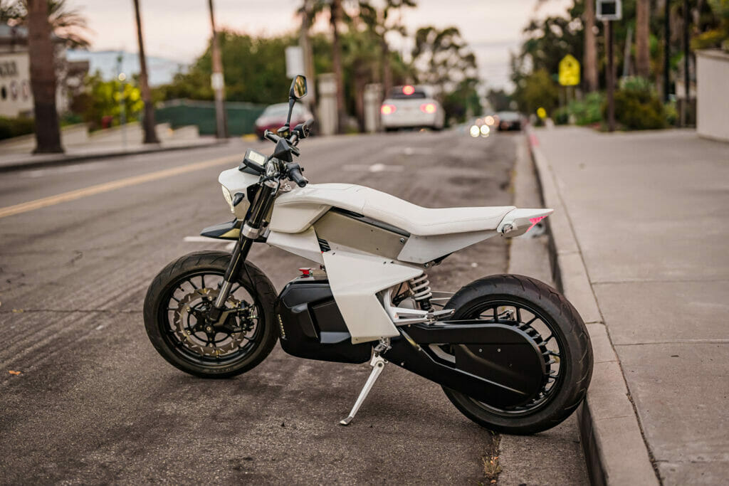 A white electric motorcycle parked on the side of the street.
