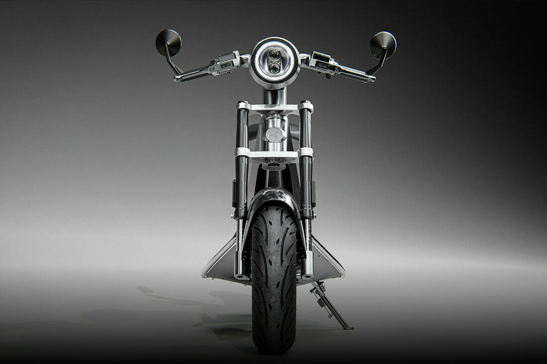 Front view of a sleek, modern motorcycle with a large headlamp, dual side mirrors, and a prominent tire. The motorcycle has metallic components and a minimalist design.